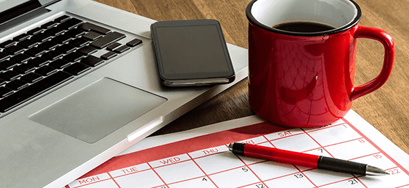 Laptop, calendar, pen, coffee cup, and cell phone on a table.