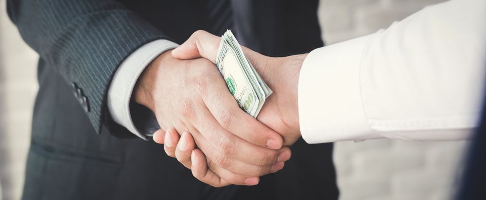 Two people exchanging money through a handshake